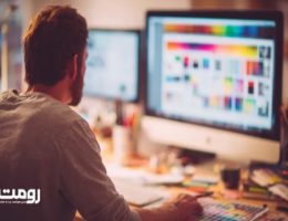 «طراح وب در حال کار روی طراحی رابط کاربری در کامپیوتر رومیزی، محیط کاری مدرن با مانیتورهای بزرگ و نور گرم، لوگوی رومت در گوشه تصویر»